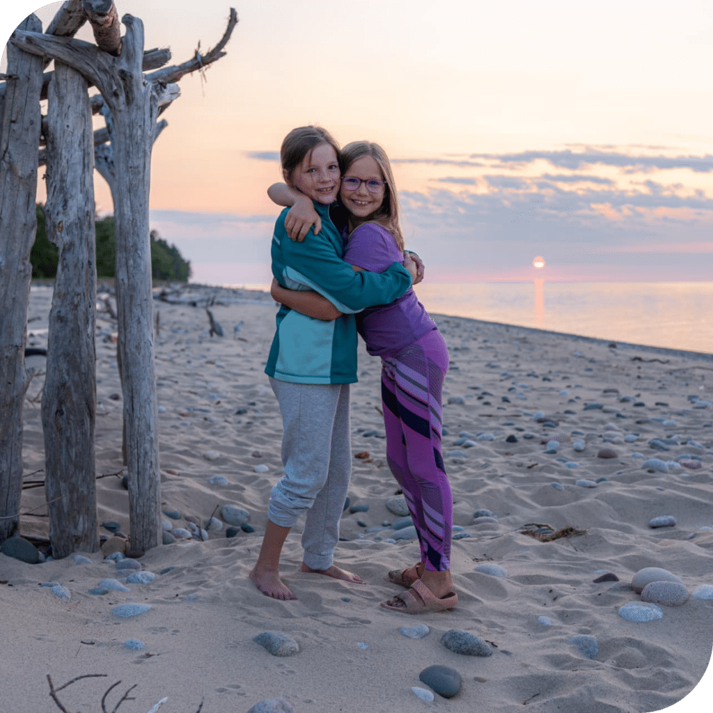 Two children hugging in front of a sunset on Sand Point Beach