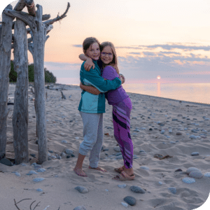 Two children hugging in front of a sunset on Sand Point Beach